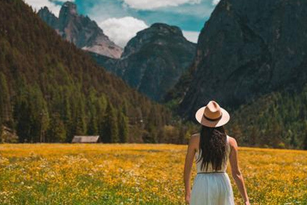 Woman in hat, standing in golden field with mountains in the background