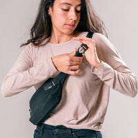 woman on light gray background buckling black sling bag across the front of her body