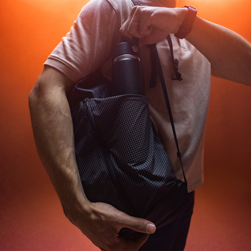 man in smoky, orange lit studio, pulling water bottle out of edx backpack