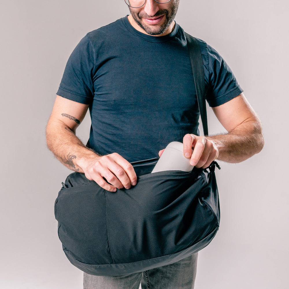 man placing water bottle in exterior pocket of black duffle