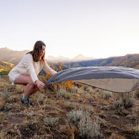 Woman in mountain sunset scene, laying down pocket blanket on dry brush