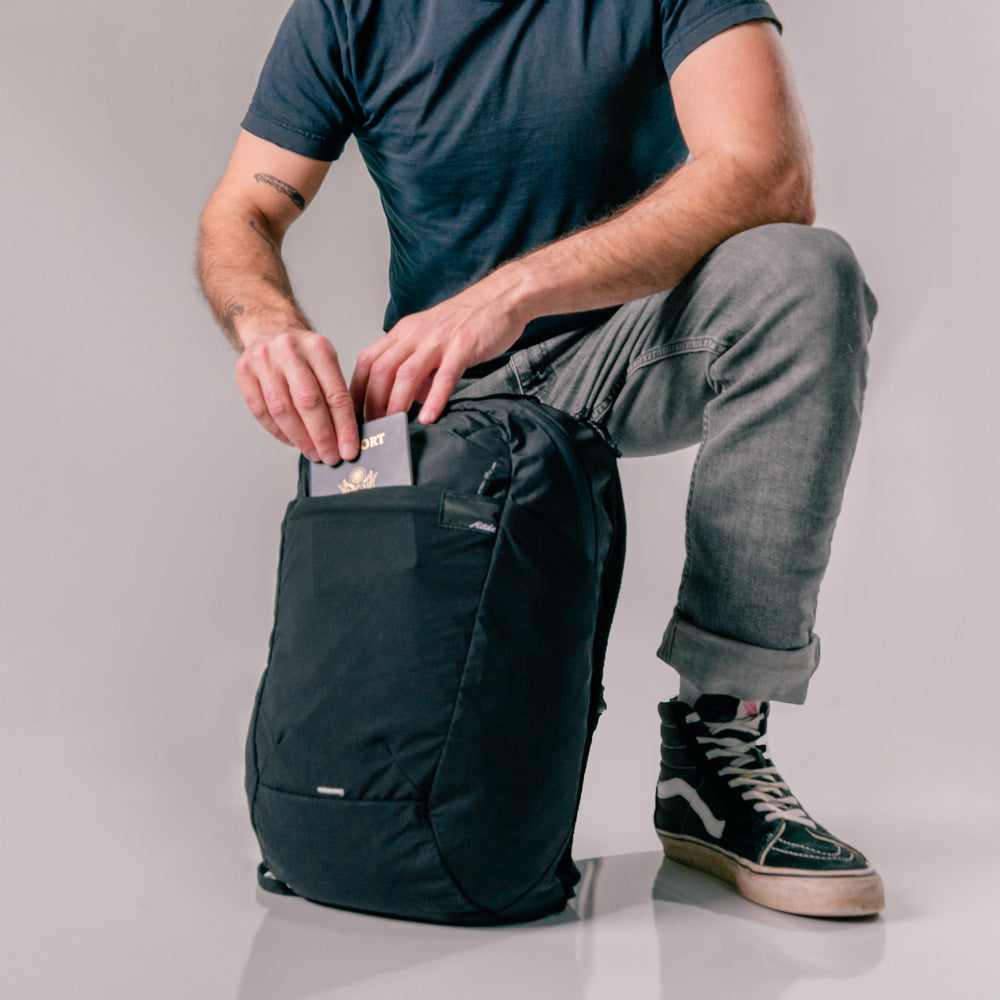 man placing passport into front pocket of black backpack