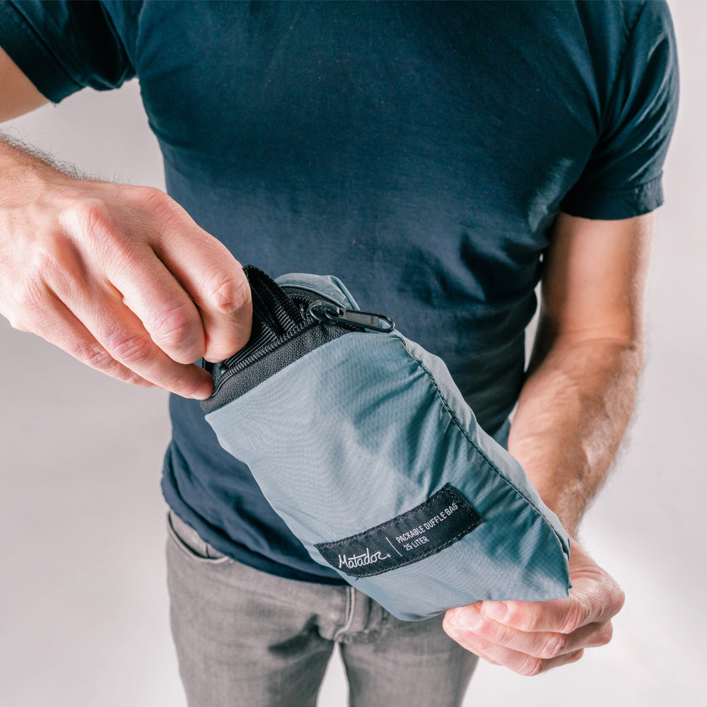 man pulling slate blue duffle out of packed down pouch