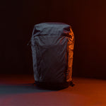 Front view of Black backpack with grid fabric in front of black background lit with orange light 