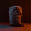 3/4 view of Black backpack with grid fabric in front of black background lit with orange light 