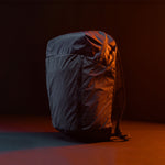 3/4 view of Black backpack with grid fabric in front of black background lit with orange light 