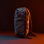 left side view of Black backpack with grid fabric in front of black background lit with orange light 