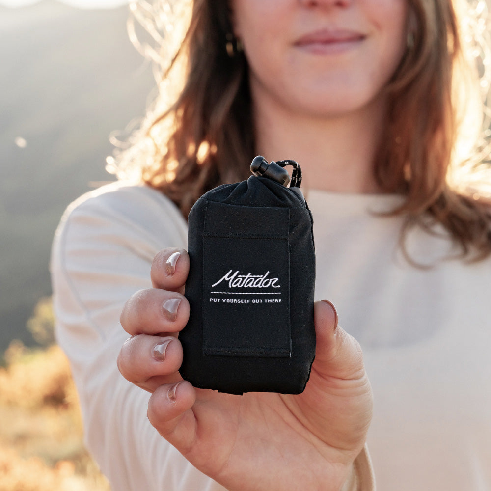 Woman in sunny setting holding black Pocket Blanket Mini to the camera