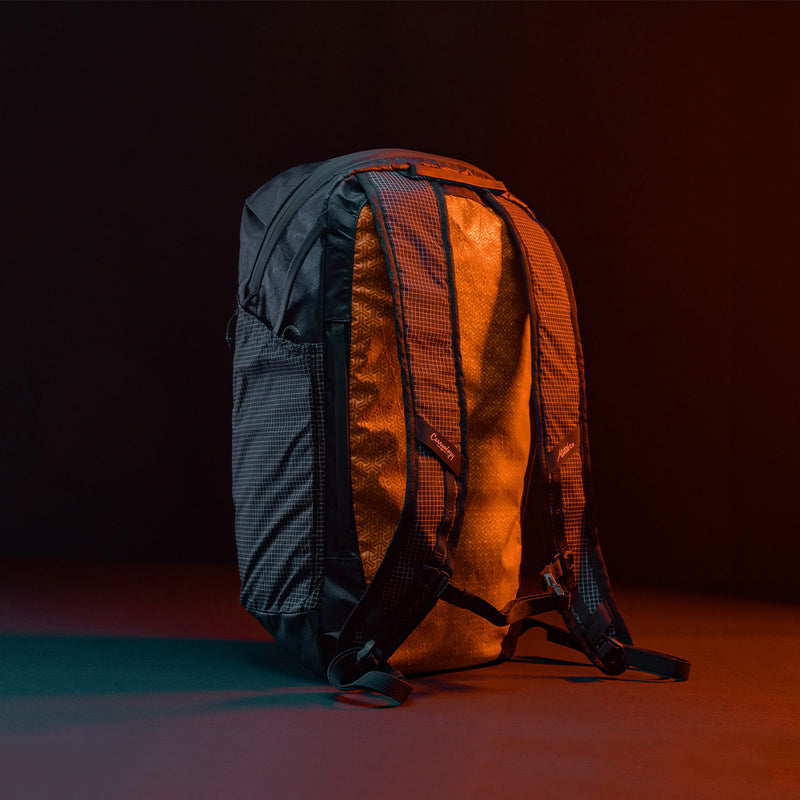 Back 3/4 view of Black backpack with grid fabric in front of black background lit with orange light 