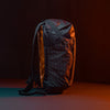 right side view of Black backpack with grid fabric in front of black background lit with orange light 