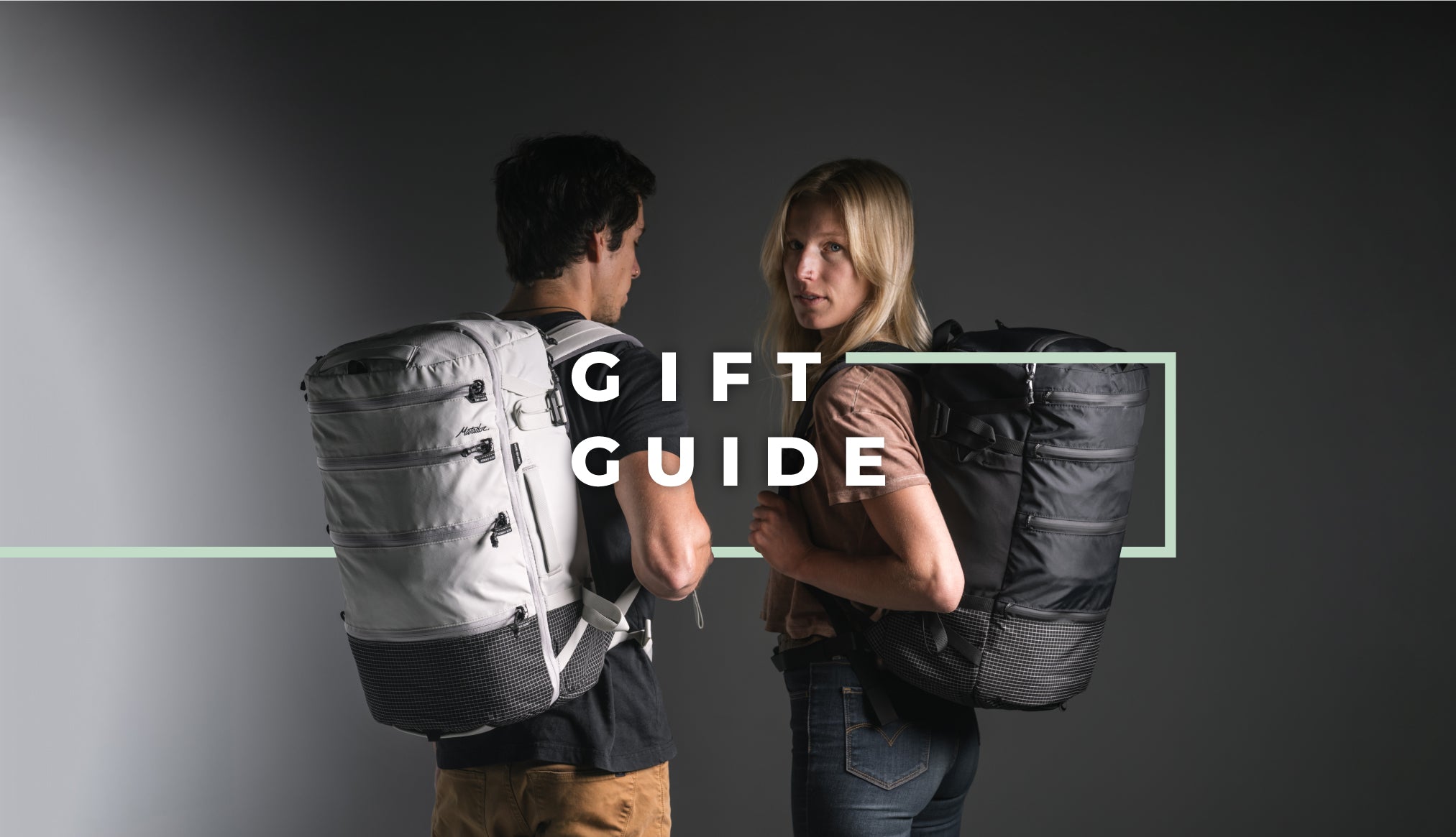 Man an woman on dark gray background wearing white and black backpacks with overlaid text "Gift Guide"