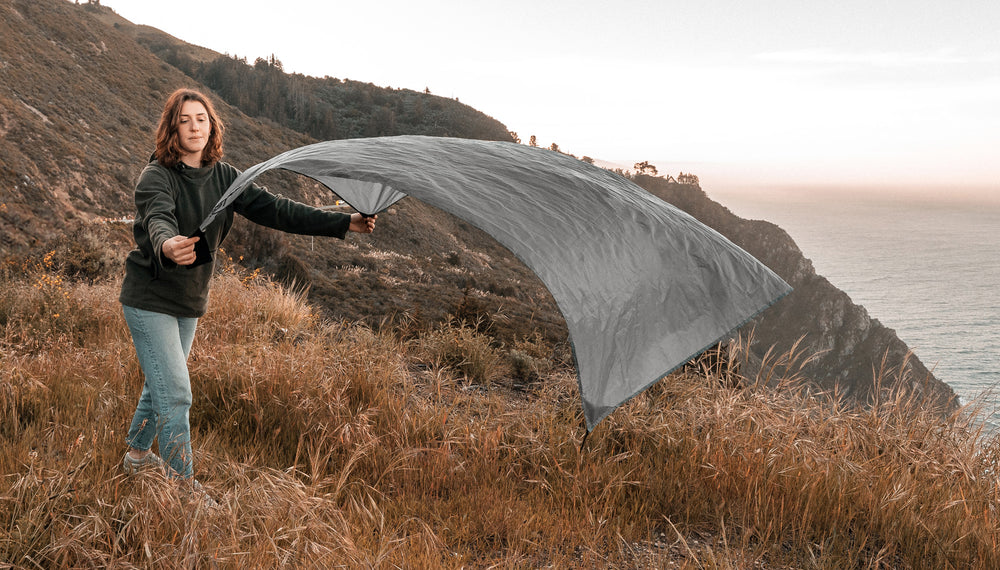 Woman laying down a pocket blanket on a grassy cliff overlooking the ocean