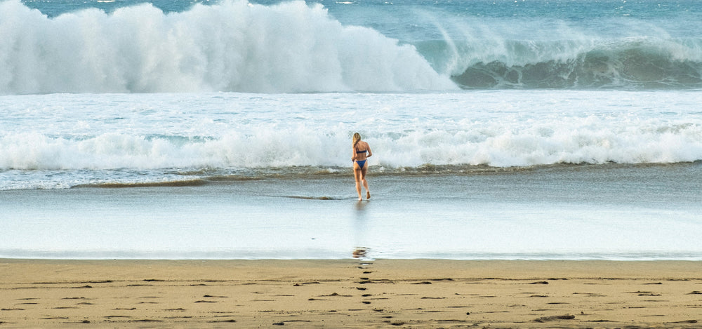 woman walking along a beach with large waves