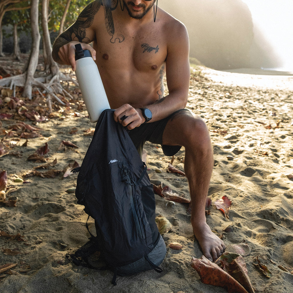 Man on a tropical beach, placing white water bottle in freerain22 backpack