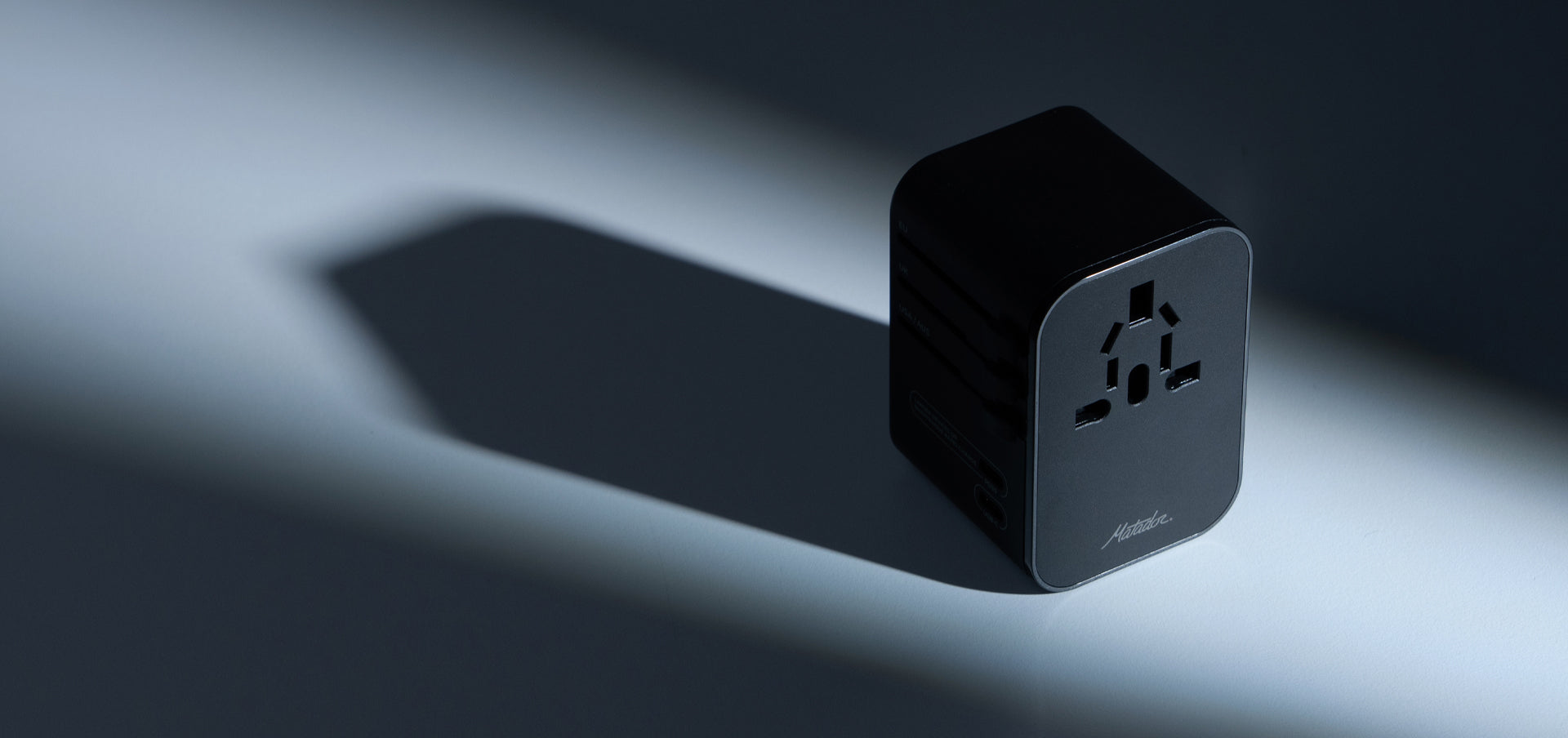 Black Global Travel Adapter on clean surface with dramatic dark shadows casted