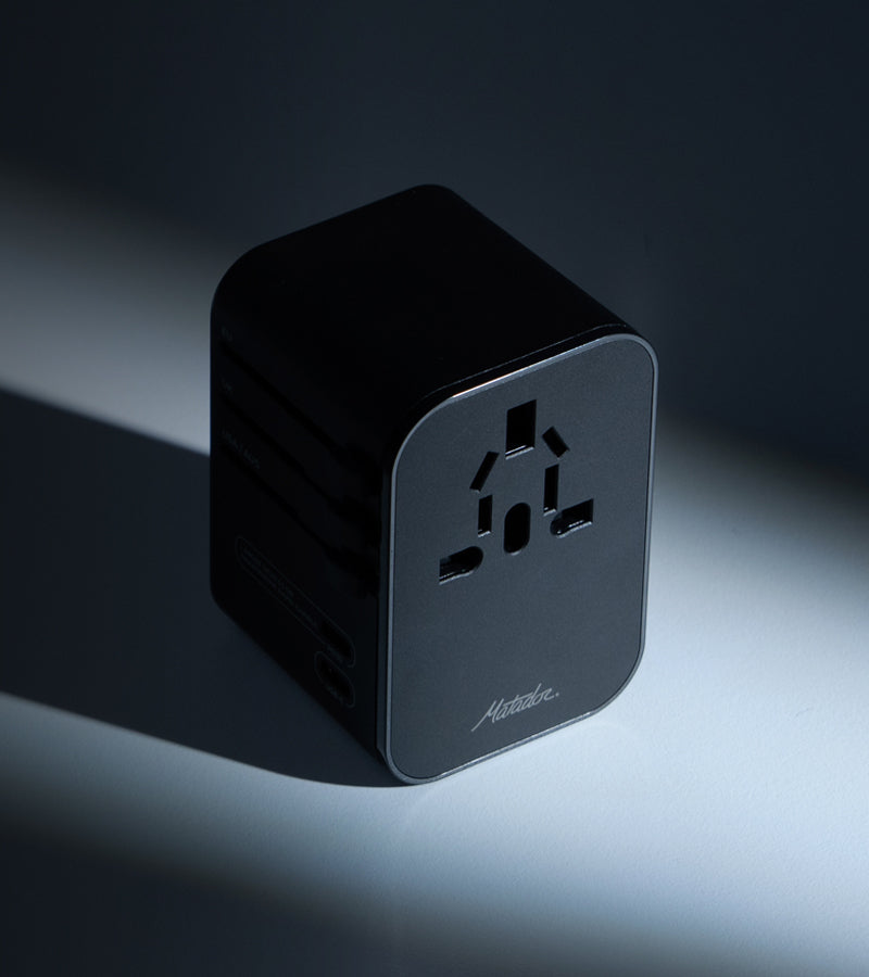 Black Global Travel Adapter on clean surface with dramatic dark shadows casted