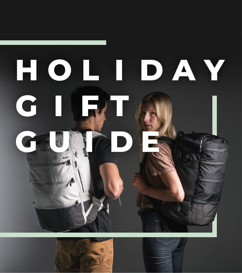 man and woman wearing black and white backpacks on dark gray background with text "holiday gift guide"