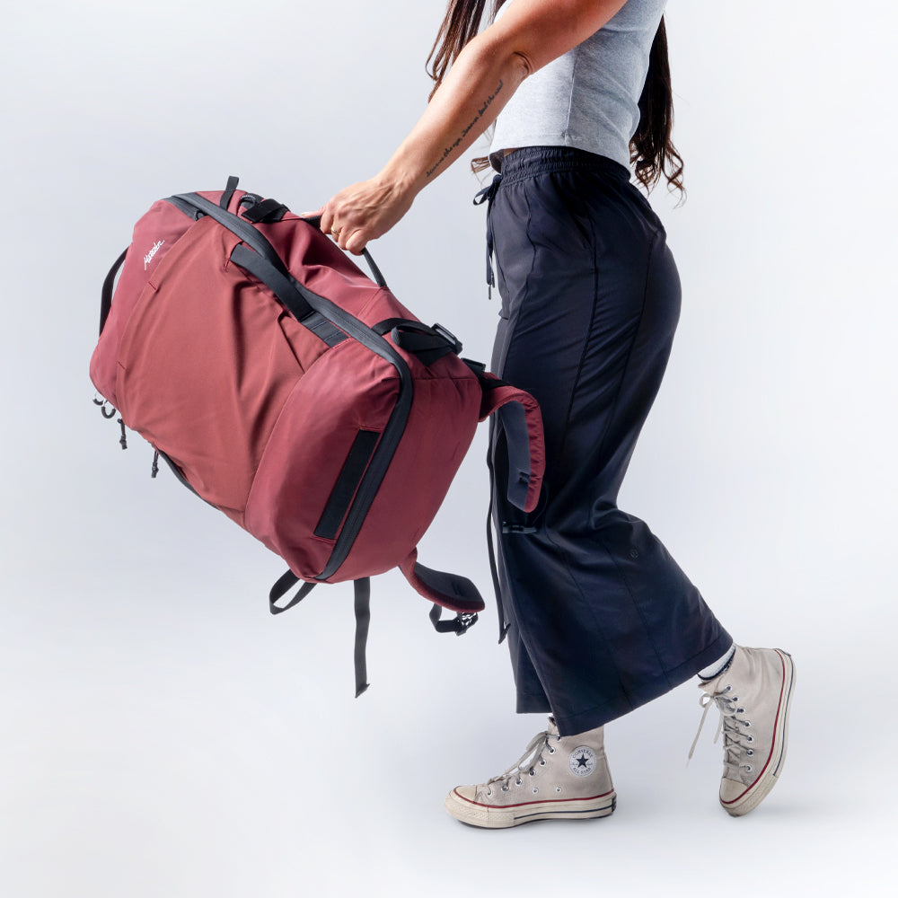 Waist down shot of woman walking on light gray background, swinging a garnet globerider35 in front of her.