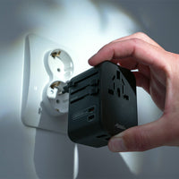 hand holding travel adapter, plugging it into an EU outlet on white wall