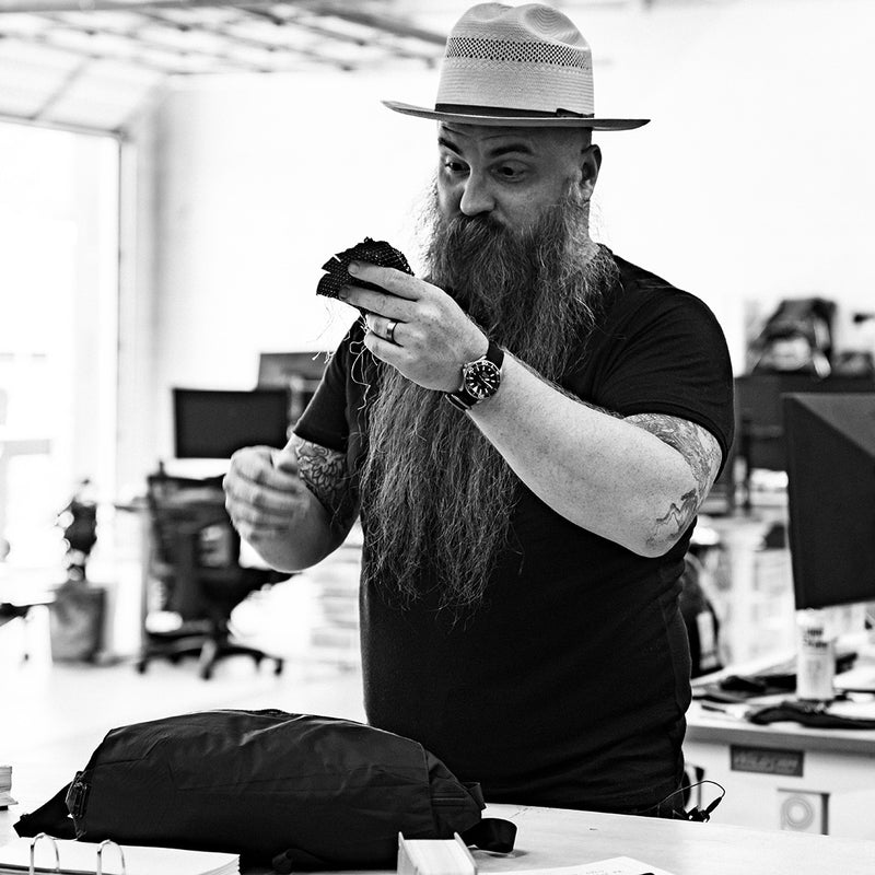 man with very long beard and hat, looking at fabric swatches