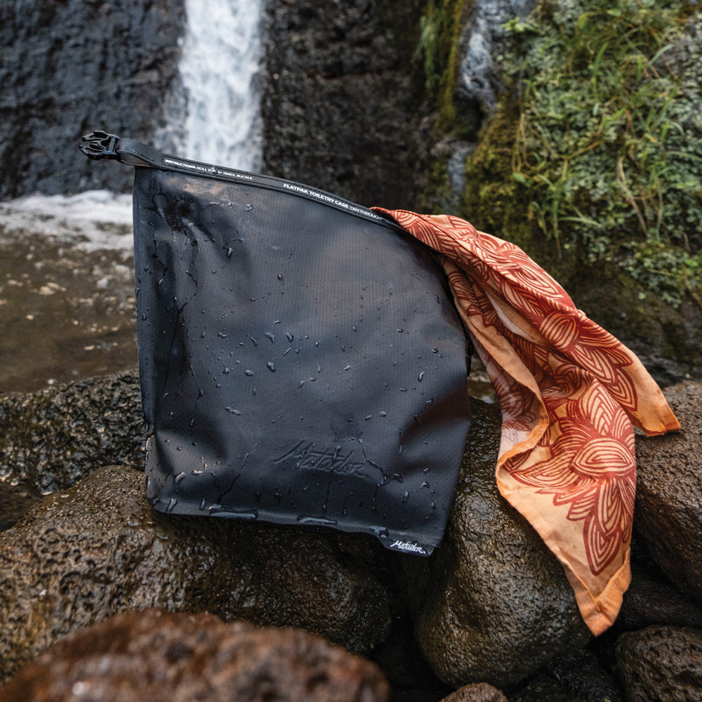 black waterproof toiletry case sitting next to tropical waterfall