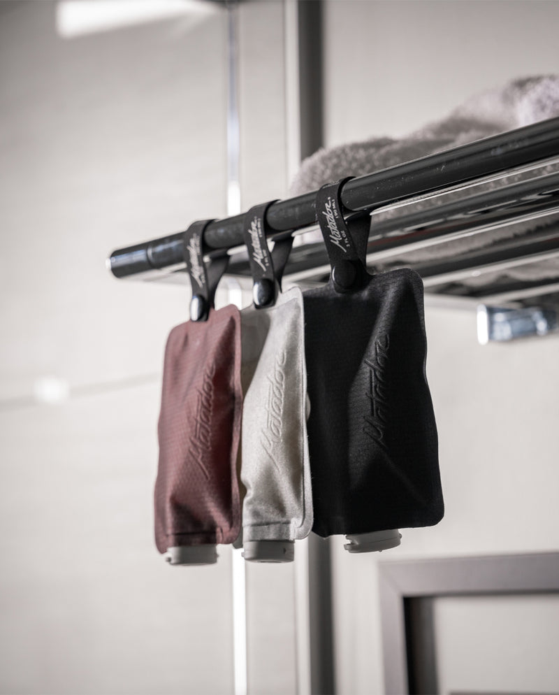 Garnet, white, and charcoal flatpak toiletry bottles hanging from bar in bathroom setting