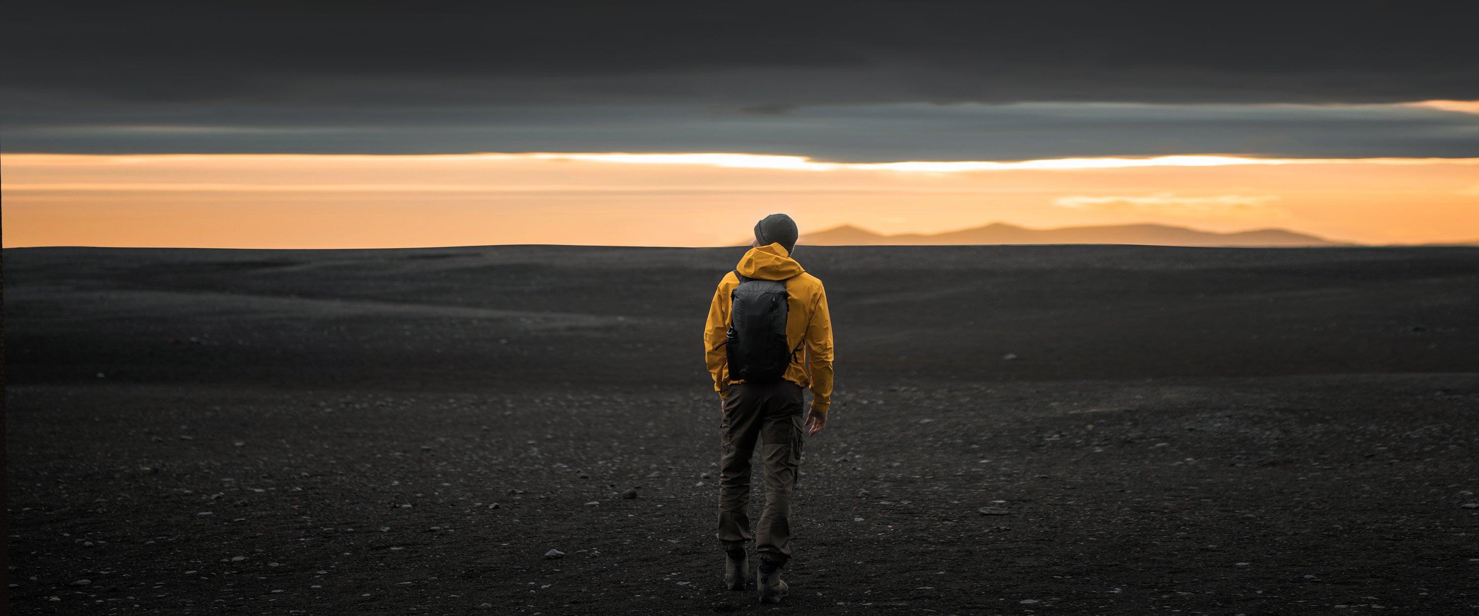 man in yellow jacket, standing in front of glowing horizon sunset