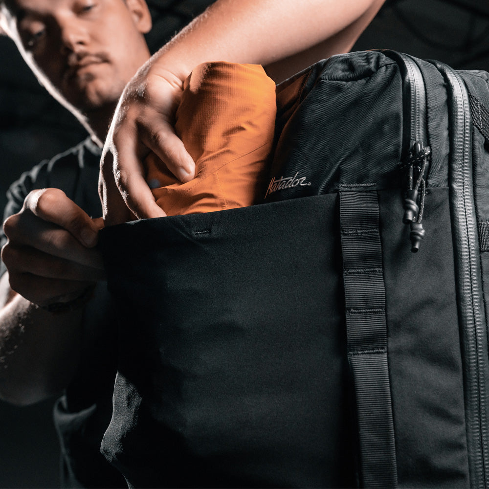 Man placing rolled up orange jacket into exterior mesh pocket