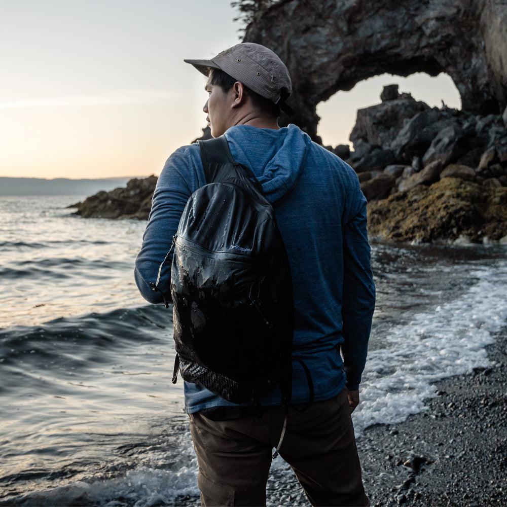 Man standing on rocky beach with backpack on one shoulder