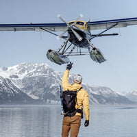 Man wearing backpack, waving to sea plan on Alaskan lake